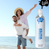 A joyful couple enjoys a sunny day at the beach, with the woman laughing as she rides on the man's back. Next to them is a large bottle labeled "Wet Water-Based Lubricant," offering stain-free, versatile pleasure. They are dressed in casual summer outfits.